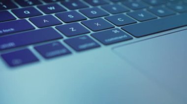 Close-up laptop keyboard with multi-colored highlights on it. Very blurry reflection of what is displayed on the monitor