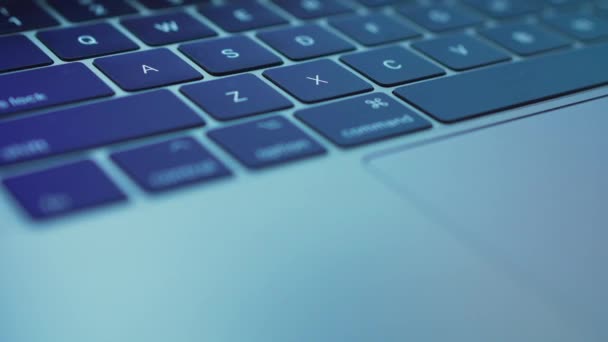 Close-up laptop keyboard with multi-colored highlights on it. Very blurry reflection of what is displayed on the monitor — Stockvideo