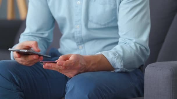 Επισήμως ντυμένος άνθρωπος κάθεται σε έναν καναπέ, επιλέξτε από πολλές πιστωτικές κάρτες και εισάγει τον αριθμό σε ένα smartphone για να πληρώσει online. Online αγορές, τεχνολογία lifestyle. Κοντινό πλάνο — Αρχείο Βίντεο