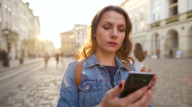 Woman stands in the middle of the square of the old city, using smartphone and takes photos of sights at sunset