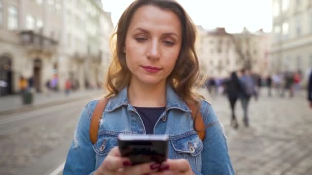 Γυναίκα περπατά σε ένα παλιό δρόμο χρησιμοποιώντας smartphone στο ηλιοβασίλεμα. Επικοινωνία, έννοια των κοινωνικών δικτύων. Αργή κίνηση — Αρχείο Βίντεο