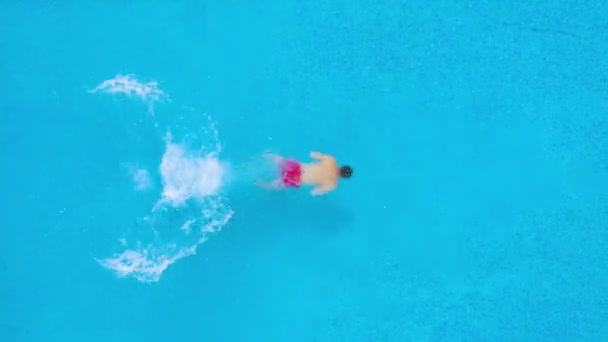 Uitzicht vanaf de top zoals een man in het zwembad duikt en zwemt onder het water — Stockvideo
