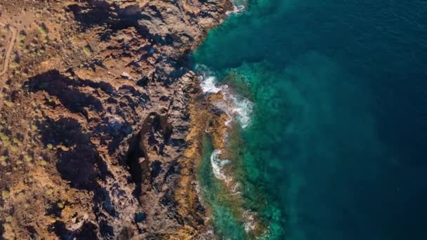 さびれた海岸のトップビュー。テネリフェ島のロッキー海岸。海岸に到達する海の波の空中ドローン映像 — ストック動画