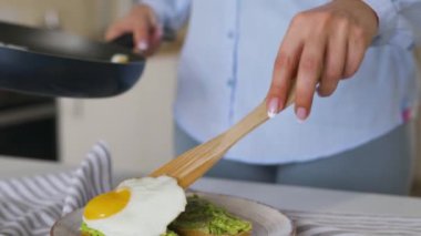 Kadın, avokado tostlu bir tabağa kızarmış yumurta koyar. Sağlıklı vejetaryen kahvaltısı.