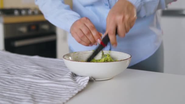 Женщина нарезает авокадо в миске, чтобы приготовить здоровый веганский завтрак — стоковое видео