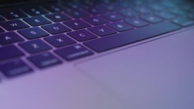Close-up laptop keyboard with multi-colored highlights on it. Very blurry reflection of what is displayed on the monitor