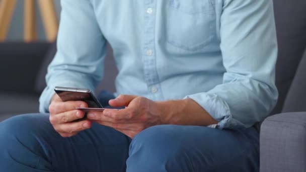 Formell gekleideter Mann sitzt auf einem Sofa, wählt aus mehreren Kreditkarten und gibt seine Nummer in ein Smartphone ein, um online zu bezahlen. Online-Shopping, Lifestyletechnologie. Nahaufnahme — Stockvideo