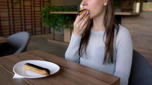 Mujer come eclair de chocolate en un café — Vídeos de Stock