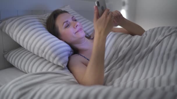 Mujer usando smartphone mientras está acostado en la cama. Se frota los ojos, porque está cansada y somnolienta. Concepto de adicto móvil o insomnio . — Vídeo de stock