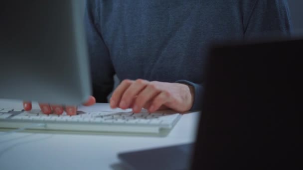 Ein männlicher Hacker unter der Haube und eine Brille, die in einem dunklen Büroraum an einem Computer arbeitet. Cybercrime-Konzept — Stockvideo