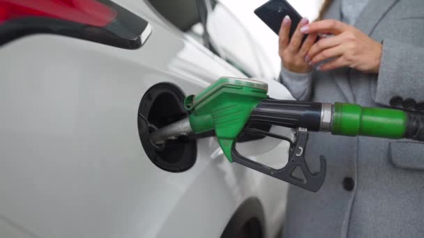 Woman using smartphone while her car is refueling. Slow motion — Stock Video