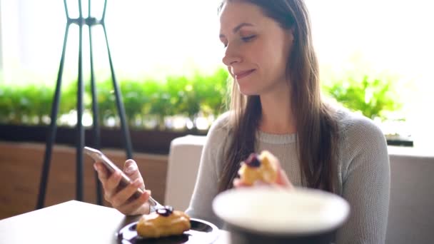 Nő eszik eclairs egy kávézóban, és egy okostelefon — Stock videók