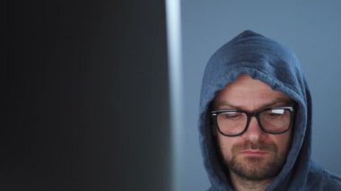 Kapüşonlu ve gözlüklü bir erkek hacker karanlık bir ofis odasında bilgisayar üzerinde çalışıyor. Siber suç kavramı