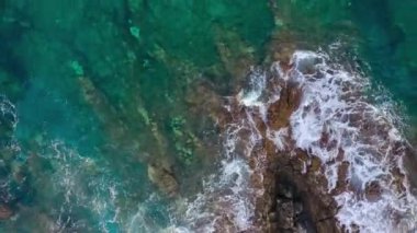 Issız bir sahil manzarası. Tenerife adasının kayalık kıyısı. Okyanus dalgalarının kıyıya ulaştığı hava aracı görüntüleri. Kamera dönüyor.