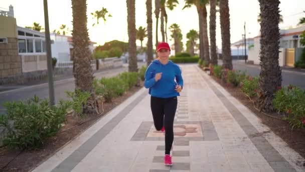 La mujer corre por la calle a lo largo de la avenida Palm al atardecer. Vida activa saludable. Movimiento lento — Vídeo de stock