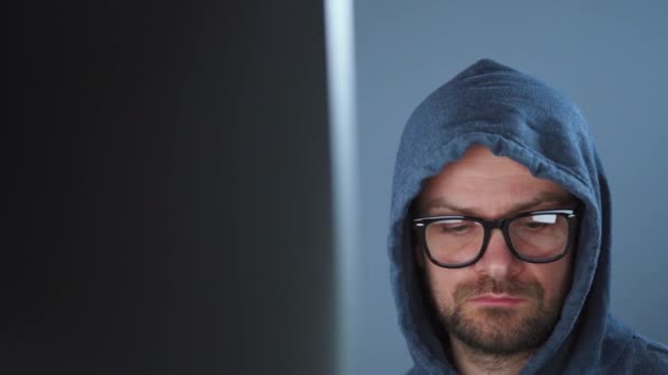 Un pirate dans le capot et des lunettes travaillant sur un ordinateur dans une pièce sombre du bureau. Concept de cybercriminalité — Video