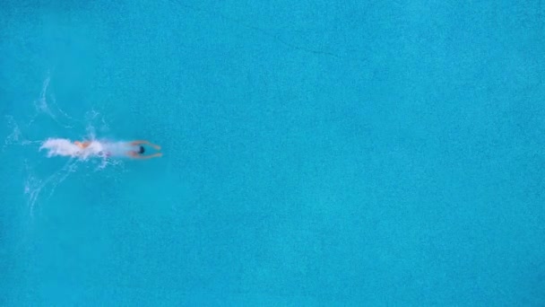 Vue du haut comme un homme plonge dans la piscine et nage sous l'eau. Mouvement lent — Video