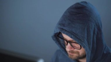 Kapüşonlu ve gözlüklü bir erkek hacker karanlık bir ofis odasında bilgisayar üzerinde çalışıyor. Siber suç kavramı
