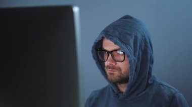 Kapüşonlu ve gözlüklü bir erkek hacker karanlık bir ofis odasında bilgisayar üzerinde çalışıyor. Siber suç kavramı