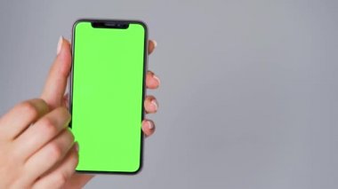 Gri arka planda yeşil ekranlı akıllı telefon kullanan kadın eller. Krom anahtar