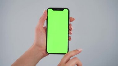 Gri arka planda yeşil ekranlı akıllı telefon kullanan kadın eller. Krom anahtar