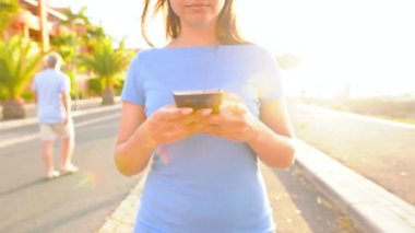 Gün batımında Palm Street 'te yürürken mavi elbiseli bir kadın akıllı telefon kullanıyor.