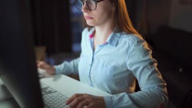 Gözlüklü kadın monitöre bakıyor ve internette sörf yapıyor. Monitör ekranı gözlüklere yansıyor. Gece çalış. İçişleri Bakanlığı. Uzak çalışma