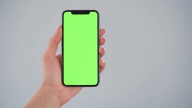 Gri arka planda yeşil ekranlı akıllı telefonu tutan kadın eller. Krom anahtar. Boşluğu Kopyala