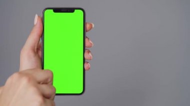 Gri arka planda yeşil ekranlı akıllı telefon kullanan kadın eller. Krom anahtar