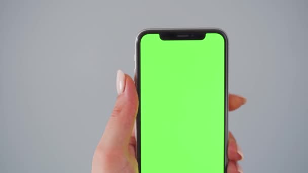 Manos femeninas usando un smartphone con una pantalla verde sobre un fondo gris. Clave de croma — Vídeo de stock