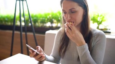 Bir kafede eklem yiyen ve akıllı telefon kullanan bir kadın.