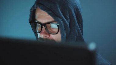 Kapüşonlu ve gözlüklü bir erkek hacker karanlık bir ofis odasında bilgisayar üzerinde çalışıyor. Siber suç kavramı