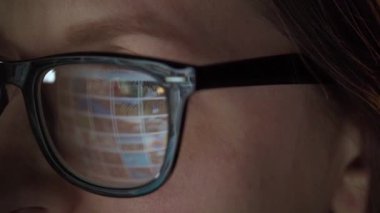 Gözlüklü kadın monitöre bakıyor ve internette sörf yapıyor. Monitör ekranı gözlüklere yansıyor. Hem de çok yakından. Gece çalış. İçişleri Bakanlığı. Uzak çalışma