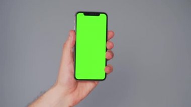 Gri arka planda yeşil ekranlı akıllı telefon kullanan erkek eller. Krom anahtar