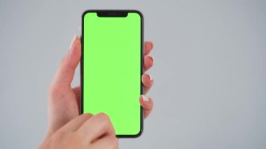 Gri arka planda yeşil ekranlı akıllı telefon kullanan kadın eller. Krom anahtar. Boşluğu Kopyala