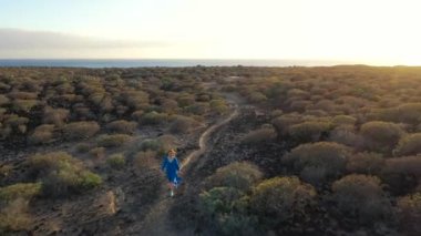 Güzel mavi elbiseli bir kadının hava manzarası gün batımında doğa koruma alanında yürüyor. Tenerife, Kanarya Adaları, İspanya