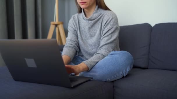 Egy nő ül egy kényelmes kanapén, és egy laptopon dolgozik. A távmunka fogalma. — Stock videók