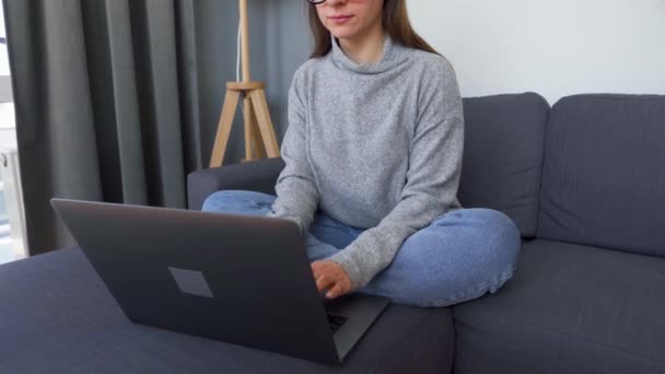 Egy nő ül egy kényelmes kanapén, és egy laptopon dolgozik. A távmunka fogalma. — Stock videók