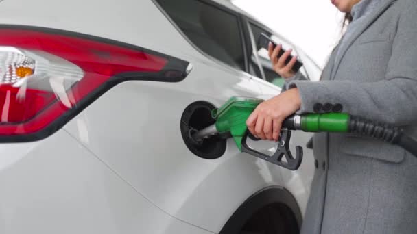 Mujer usando smartphone mientras su coche está repostando. Movimiento lento — Vídeos de Stock