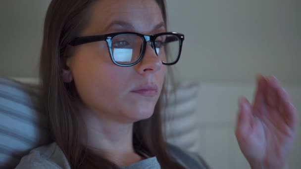 Mujer con gafas trabajando en el portátil mientras está acostada en la cama por la noche. Se frota los ojos, porque está cansada y somnolienta. Concepto de aumento del estrés y la fatiga . — Vídeo de stock