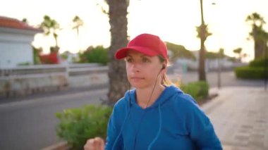 Kulaklıklı bir kadın gün batımında Palm Bulvarı boyunca koşuyor. Sağlıklı aktif yaşam biçimi