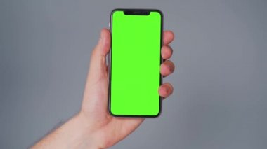 Gri arka planda yeşil ekranlı akıllı telefon kullanan erkek eller. Krom anahtar