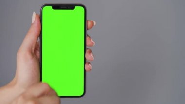 Gri arka planda yeşil ekranlı akıllı telefon kullanan kadın eller. Krom anahtar. Boşluğu Kopyala