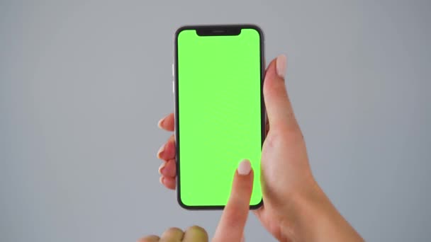 Weibliche Hände mit einem Smartphone mit grünem Bildschirm auf grauem Hintergrund. Chroma-Schlüssel. — Stockvideo