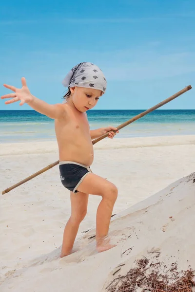 Liten pojke med en pinne på en tropisk strand — Stockfoto