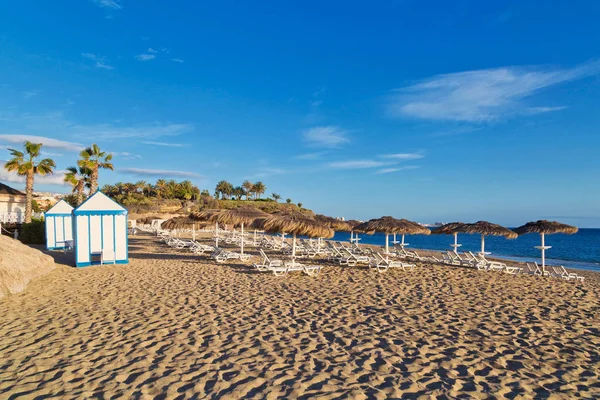 Plage de sable avec parasols au toit de chaume et chaises longues — Photo