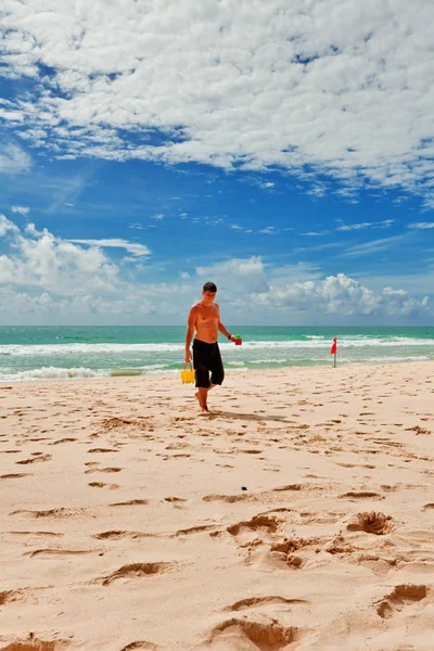 Homme avec un seau jouet jaune marche atl plage — Photo