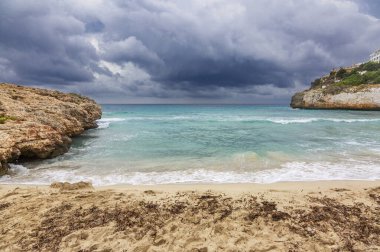 Kasvetli bir dramatik gökyüzü altında kayalık plaj