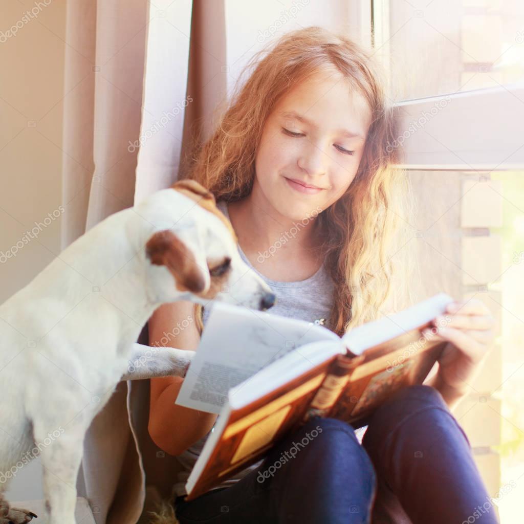 Girl reading book at home with dog