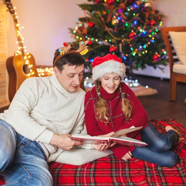 Lächelndes Mädchen mit Papa liest Buch in der Nähe von Weihnachtsbaum zu Hause — Stockfoto